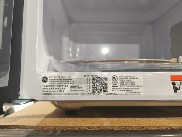 BRAND NEW SCRATCH AND DENT GE 1.1 cu. ft. countertop microwave oven, model GCST11N1WSS. Serial AA226831A, made January 2025. Tags show warranty and safety info.