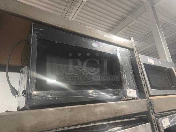 BRAND NEW GE 1.6 cu ft Over-the-Range Microwave, Model JVM3160DFBB, with minor scratches and dents, on warehouse shelf.