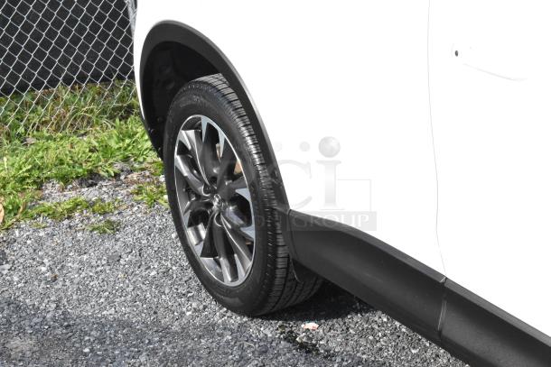 2016 Mazda CX-5 Grand Touring 4WD in white, key included. Close-up of rear wheel and tire on gravel surface.