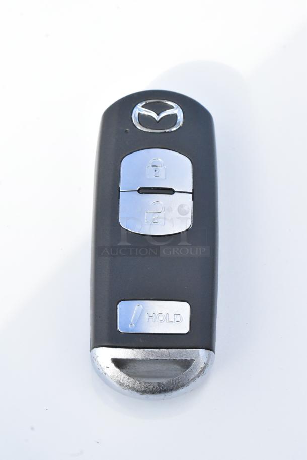 Mazda CX-5 key fob with silver buttons for lock, unlock, and hold functions, featuring the Mazda logo.