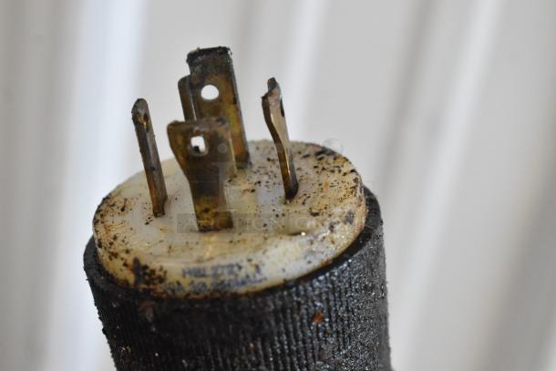 Close-up of a weathered electrical plug with visible dirt and corrosion on metal prongs.