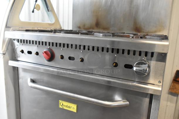Qualite stainless steel commercial gas range with 6 burners, oven, overshelf, and backsplash; visible branding and control knobs.