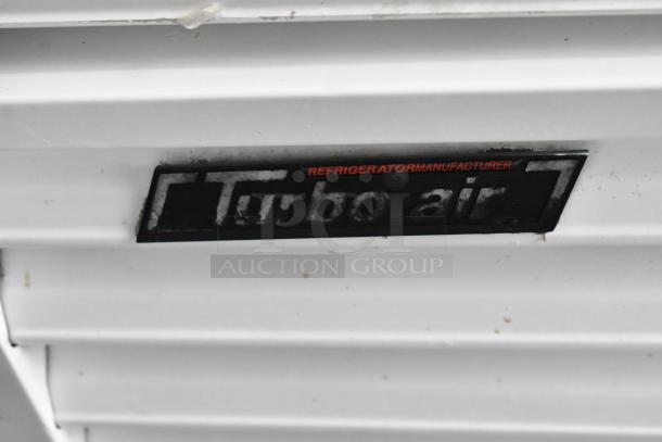 Turbo Air TGF-49F commercial freezer logo badge, indicating brand and model. White metal surface with some wear.