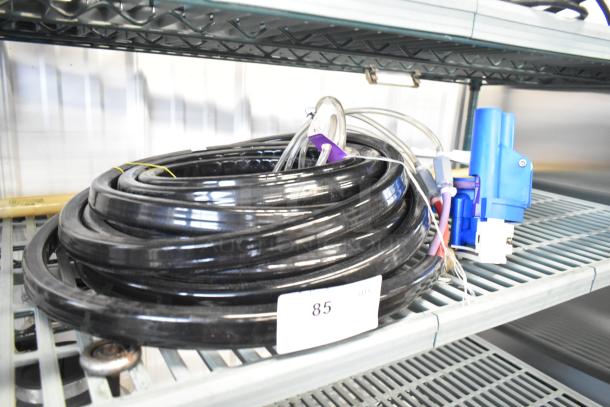 Black coiled hose with blue attachment, resting on metal shelf. Tag labeled "85" visible. Good condition.