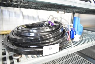 Black coiled hose with blue attachment, resting on metal shelf. Tag labeled "85" visible. Good condition.