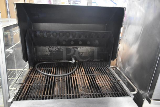 Bakers Pride stainless steel propane charbroiler grill with cover on commercial casters, showing grate and propane connection.