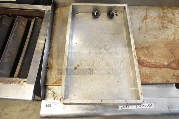 Stainless steel propane gas flat top griddle, commercial countertop model, visible wear, two control knobs, "Works" label.