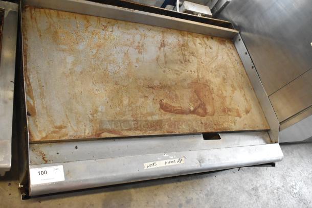 Stainless steel commercial countertop propane gas griddle, flat top, showing signs of wear. Marked "works propane" with auction tag "100 QTY 1."