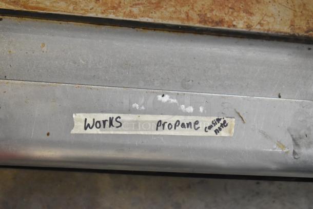 Stainless steel commercial countertop propane flat top griddle, tape label reads "Works propane".