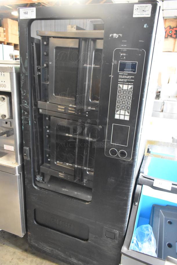 Metal commercial floor-style vending machine with card keypad. Shows signs of use. For storing and dispensing snacks.