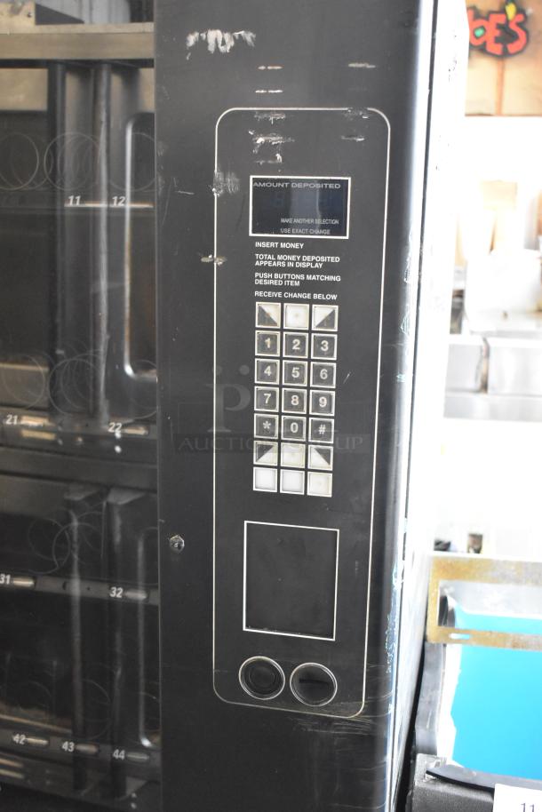 Metal commercial floor-style vending machine with keypad, coin slot, and product numbers. Signs of wear on surface.