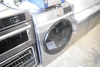 Samsung DVE45B6300P metal front load dryer, 120/240 volts, 1 phase. Silver finish, large capacity, minimal wear visible.