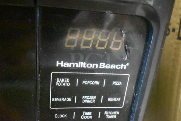 Close-up of Hamilton Beach microwave oven control panel, showing multiple cooking presets and digital display. The surface has slight wear.
