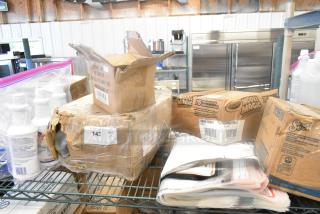 Eight various items including toilet bowl cleaner, Zebra labels, and plates in partially opened boxes on a metal shelf. Auction lot with visible tags.
