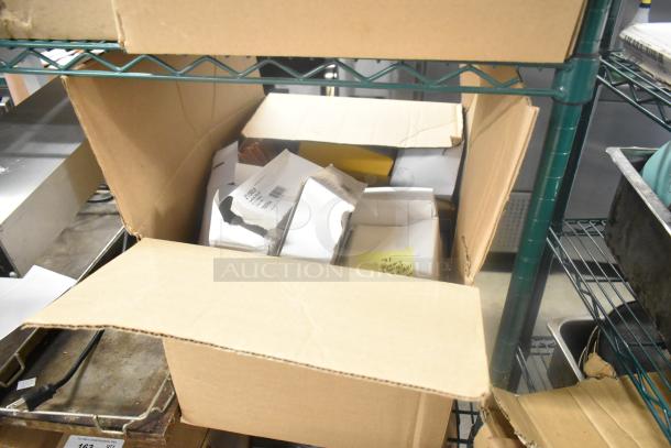 Box of assorted items including Cardinal index cards, open box, various packages visible, stored on metal shelving unit.