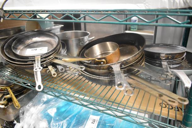 16 assorted metal skillets and stock pot on a shelf, used condition. Bid covers all items.
