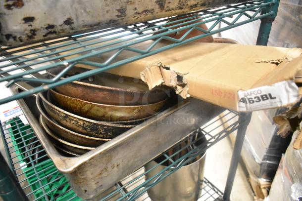 Eight assorted kitchen items including metal skillets in used condition, stored on a metal rack with a battered cardboard box labeled "AFCO 463BL".
