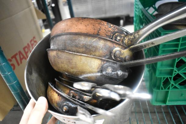 Lot of vintage metal skillets stacked in a container; visible wear and patina. Includes various sizes with metal handles.