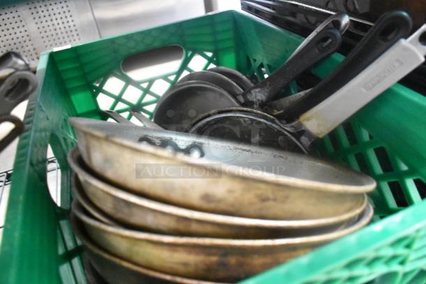 Green crate filled with various metal skillets, including visibly used pan handles.