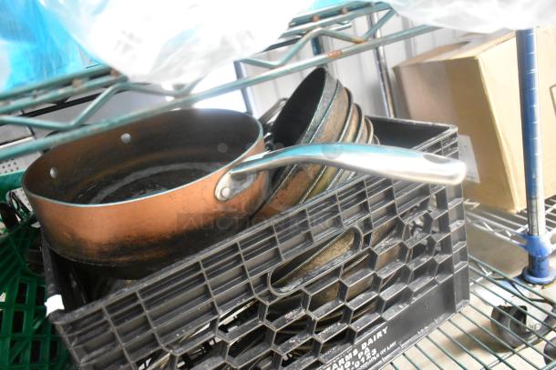 A collection of metal skillets in varying sizes, showing signs of use, stacked in a black plastic crate.