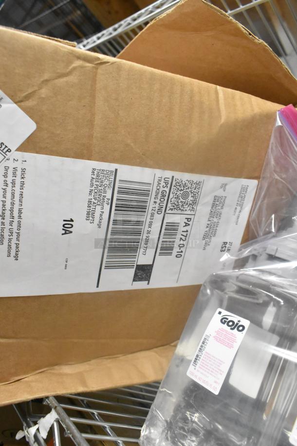 Box with UPS label, GoJo foam handwash bottle, items on metal shelf. Includes carbonless rolls and Scott dispenser.