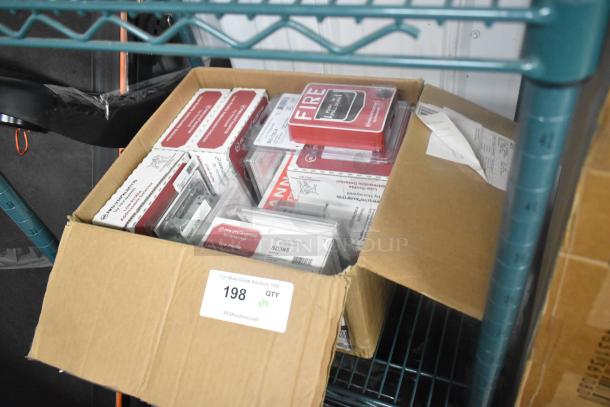 Box containing 10 fire alarm pull down boxes, multiple brands. Includes packaging with fire safety labels. Auction item 198.