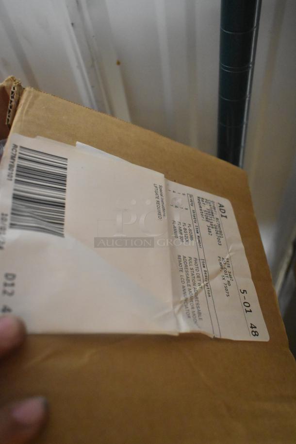 Cardboard box with shipping label listing various fire alarm models, including pull stations. Includes a bar code and ADI logo.