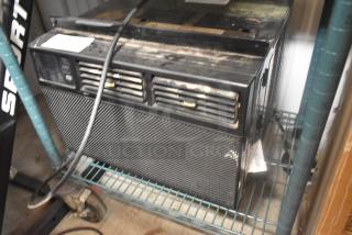 2022 window mount air conditioner, black, visible scratches and wear on casing, displayed on a metal shelf.