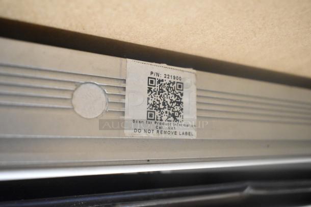Metal piece with a QR code label marked P/N: 221900, Cat: NX1, features grooves and a "Do Not Remove Label" warning.