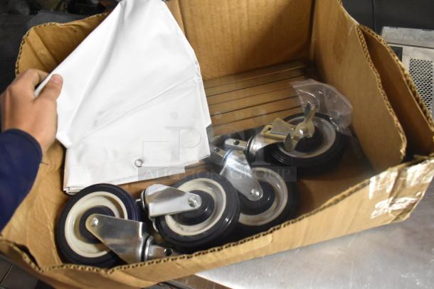 Lot of 4 commercial casters in a cardboard box, featuring metal frames and black rubber wheels, new condition.