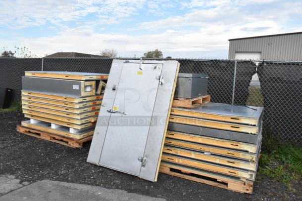 Norlake self-contained walk-in cooler parts, including door and panels, stacked on pallets outdoors. Door features labels and latch.