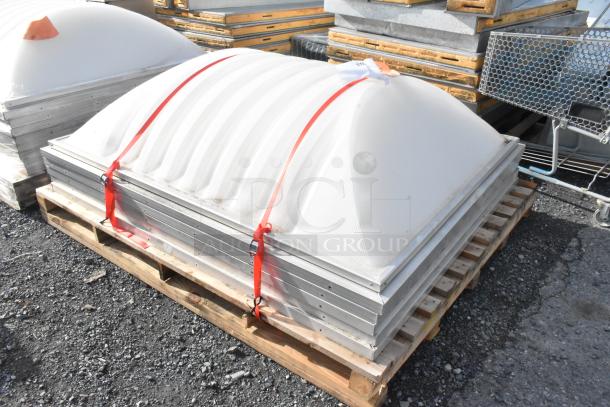 Rectangular dome cover with frosted surface, secured on a pallet with red straps. Stacked under similar covers, showing robust construction. Tags indicate auction details.