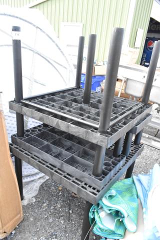 Stacked black poly tables in good condition, with grid surfaces and cylindrical legs, next to rolled blue fabric.