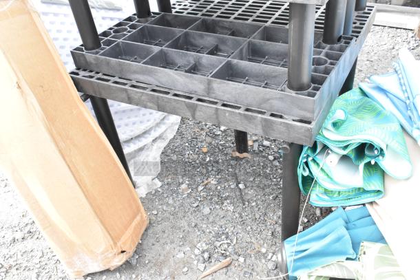 Black poly tables with grid top, sturdy legs. Includes packaging box and folded patterned materials. Outdoor condition.