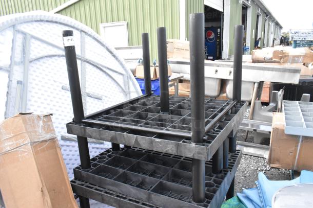 Black polyethylene tables stacked with visible grid structure, in good condition. Includes cardboard boxes and a pallet visible in the background.
