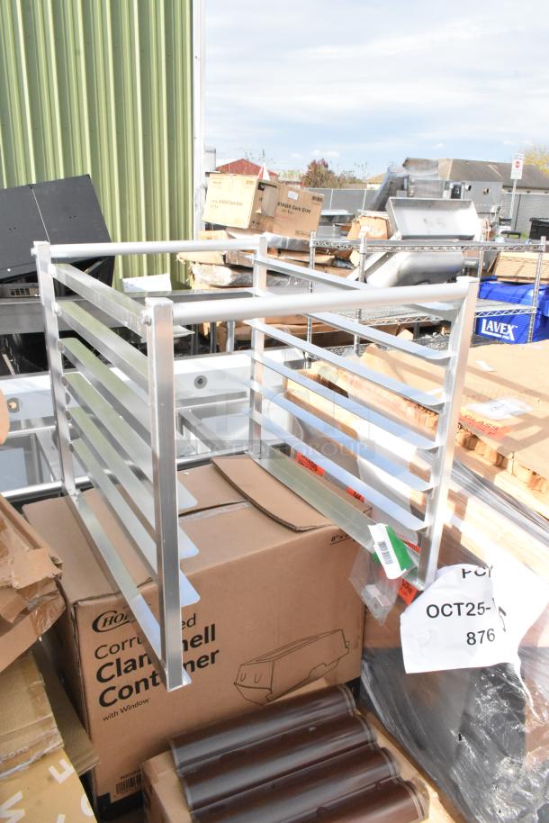Assorted new scratch and dent items including Regency aluminum bun pan rack and Nexa dispenser, visible in outdoor setup.