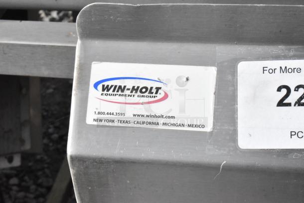 Win-holt stainless steel table with under shelf and backsplash, features brand label and contact info, in used condition.