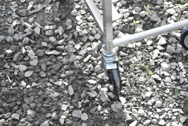 Caster wheel of Regency 600STPR20KD 20 Pan Aluminum Steam Table Pan Rack on rocky ground. Brand new with minor flaws.