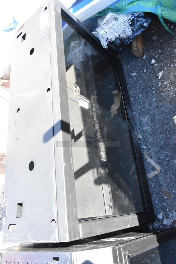 Metal 2-door cabinet, black, with clear glass panels. Shows light wear and surface scratches. Visible lock mechanism.