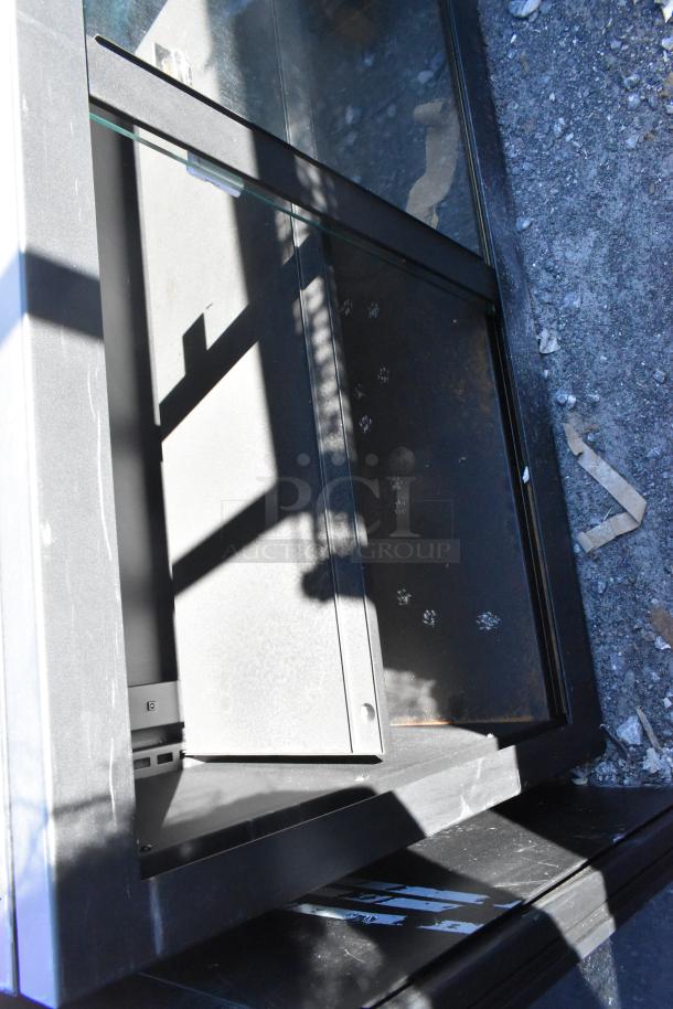 Metal 2 Door Cabinet, black finish, glass top, visible wear on surface, paw print marks.