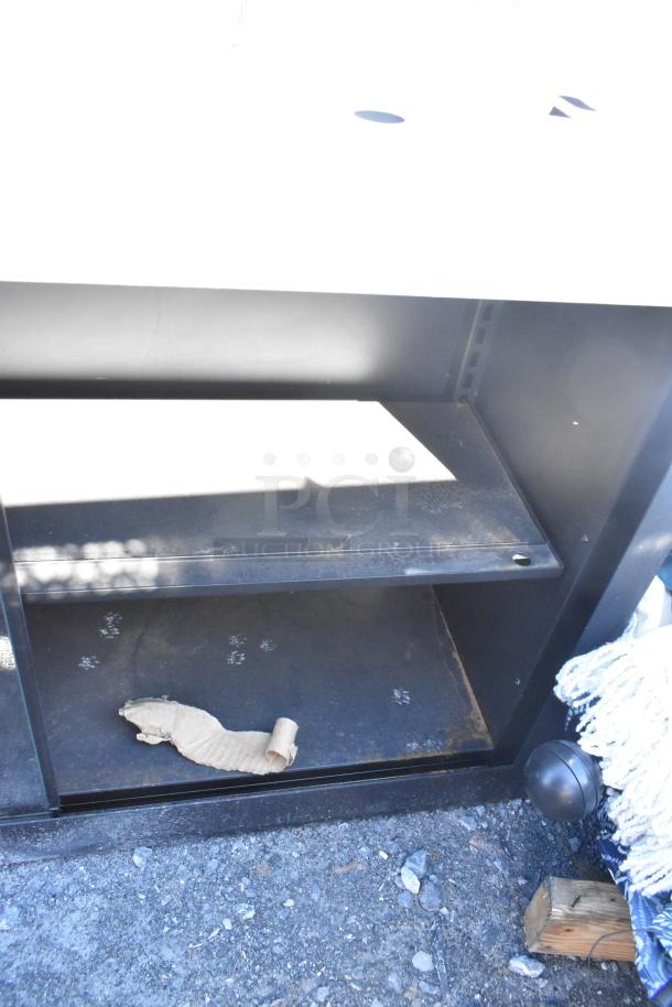 Metal 2 door cabinet with adjustable shelf, black finish, visible wear and dust. No visible labels or markings.