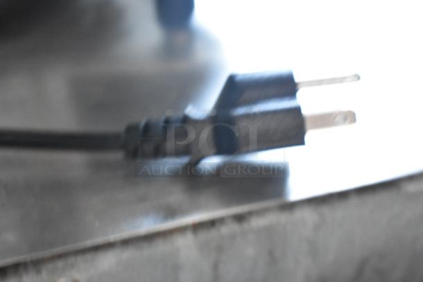 Close-up of a power plug connected to a metal surface, likely part of the 2021 Zumex Multifruit LED countertop juicer base.