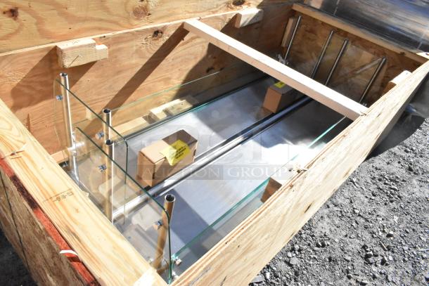 Brand new sneeze guard in wooden crate, showing glass panels and steel supports, labeled as scratch and dent.