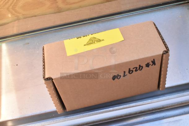 Cardboard box labeled "Advance Tabco" containing a brand new scratch and dent sneeze guard. Handwritten code on the side.