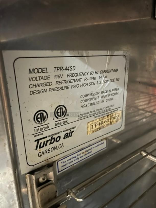 Turbo Air Super Deluxe Series TPR44SD stainless steel single door refrigerated pizza prep table, features cutting board, double overhead shelf, hotel/steamtable pan, chrome plated wire rack, 115V, on casters. Serial number TP4R603009 visible.