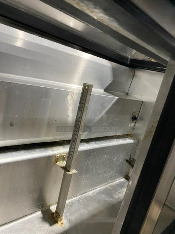 True TSSU-48-12 refrigerated prep table interior, stainless steel, visible shelves, some wear, equipped with casters.