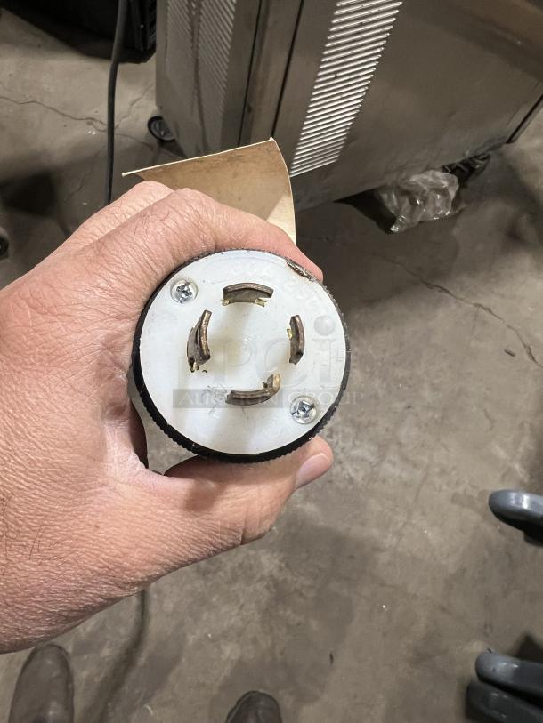 Hand holding electrical plug for Stoelting model O431-10912F-R ice cream machine, visible casters, and drip tray.
