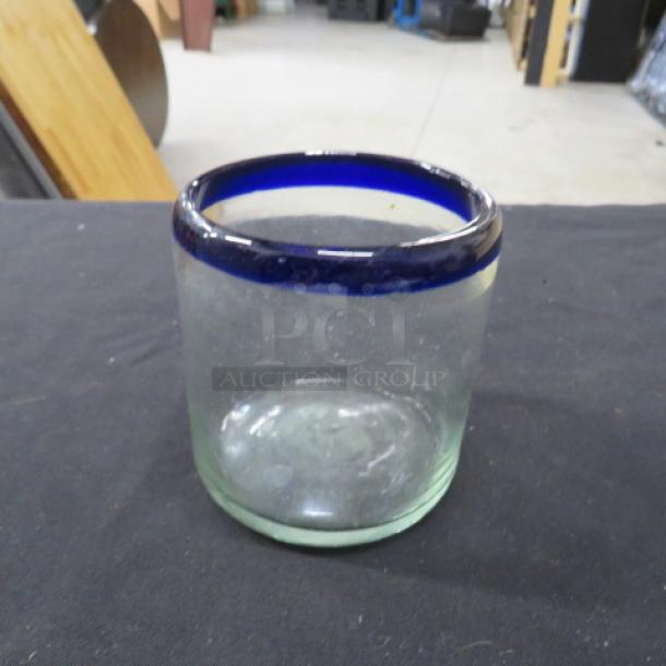 Clear glass rocks glass with blue rim, labeled 8XBID. Slightly worn condition. Simple, elegant design.