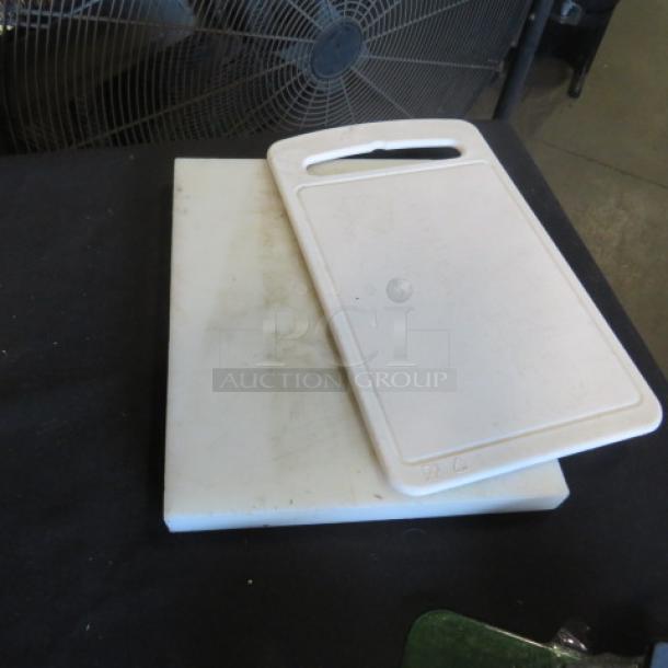 Assorted cutting boards, two white plastic pieces, one with handle, visible wear, ideal for kitchen use.