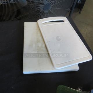 Assorted cutting boards, two white plastic pieces, one with handle, visible wear, ideal for kitchen use.